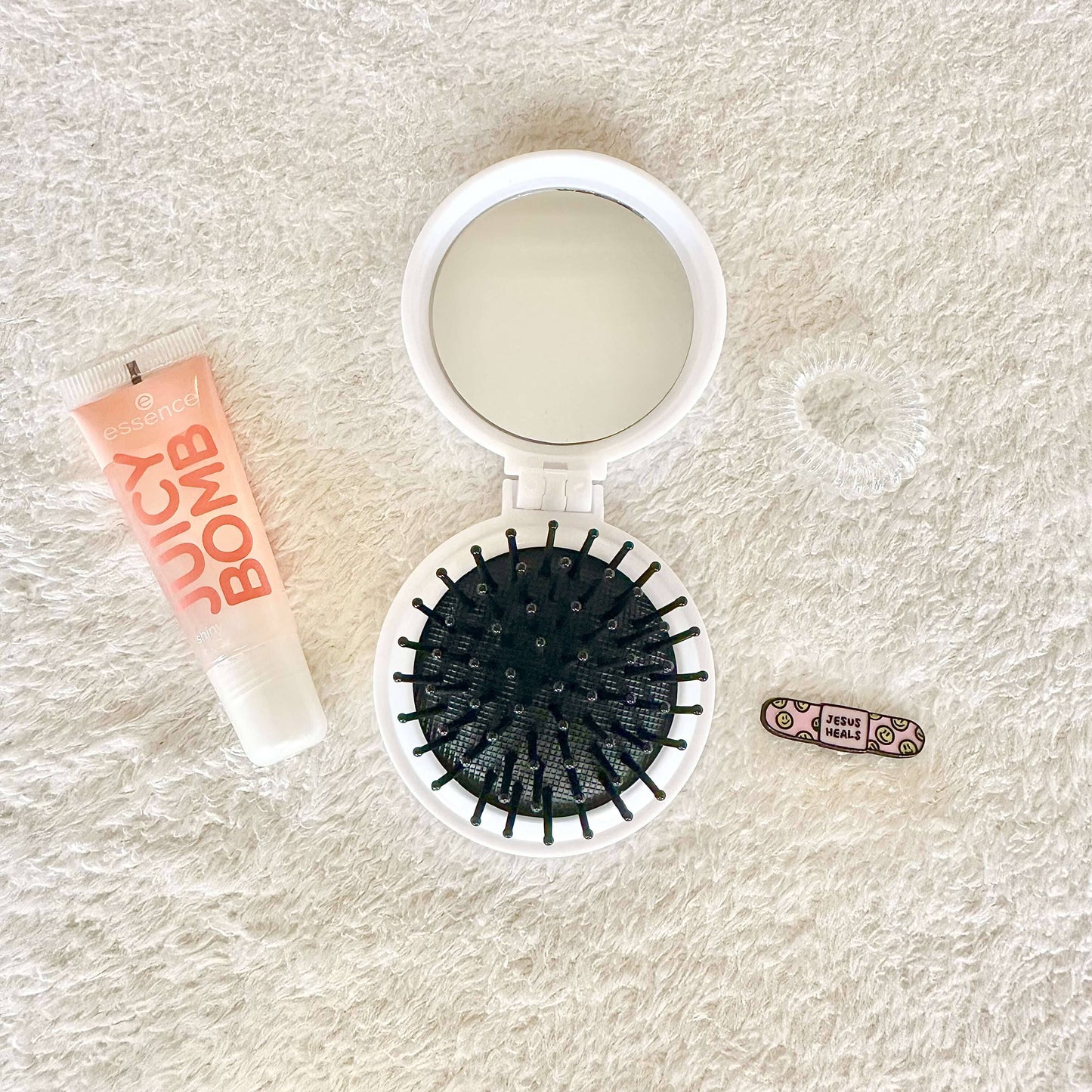 a set of a mini hairbrush, spiral hair tie, essence lipgloss, faith based mini pin